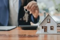 Hand holding house keys beside a small model home on a desk, symbolizing home loan requirements
